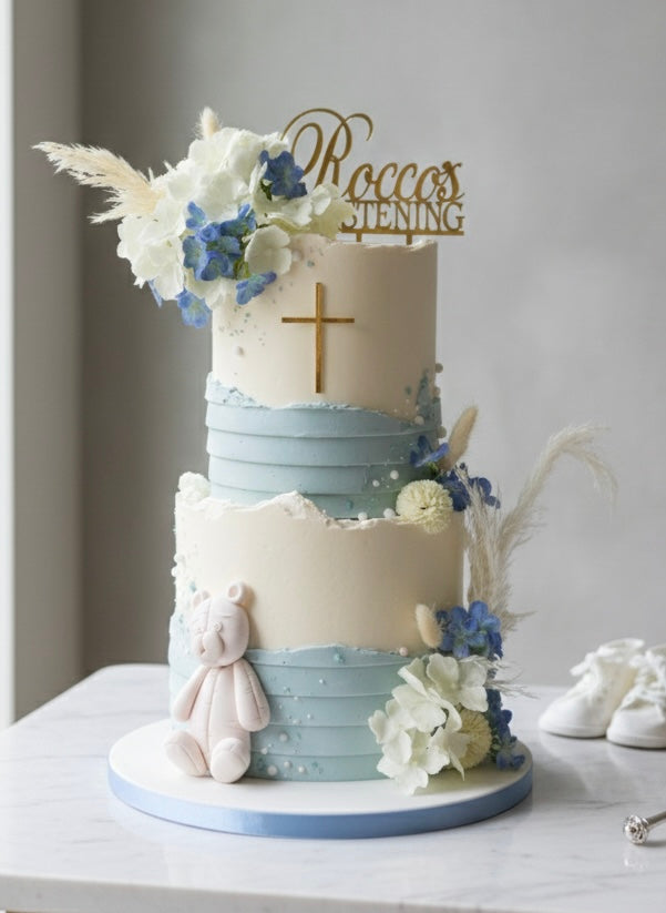Two-tiered cake with floral decorations and a cross, on a light gray background