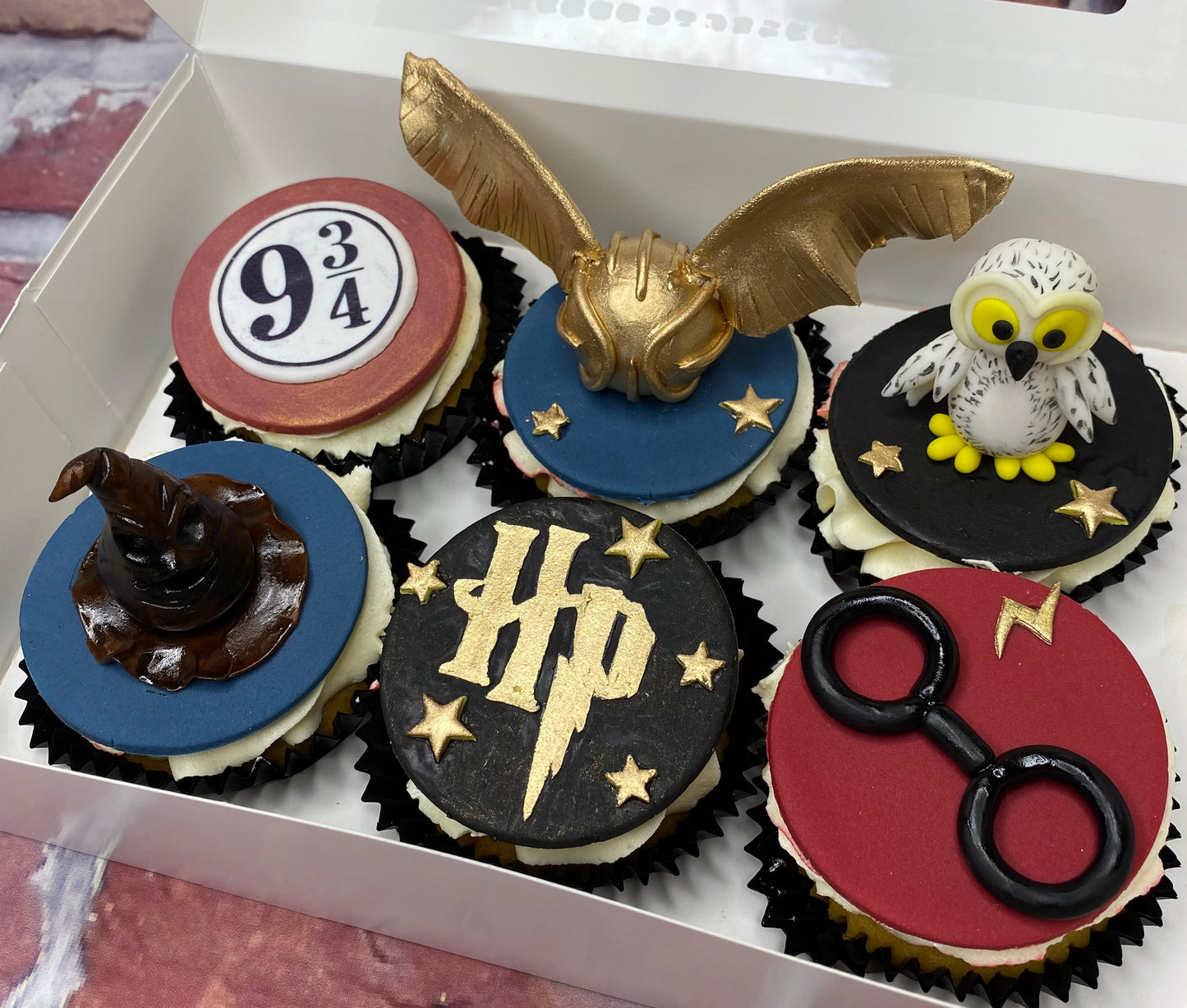 Box of Harry Potter-themed cupcakes with decorative elements.