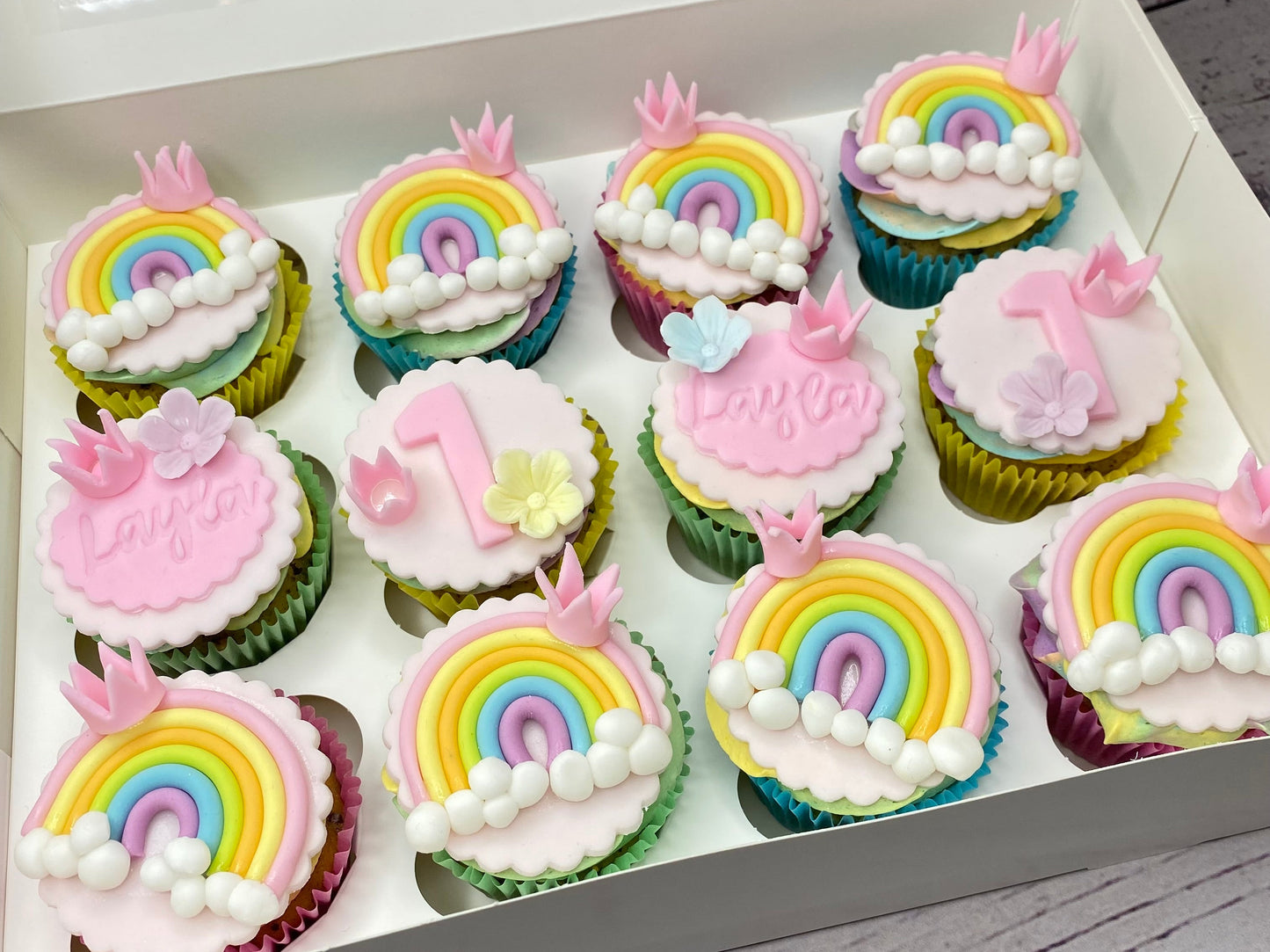Box of cupcakes with rainbow and birthday-themed decorations 
