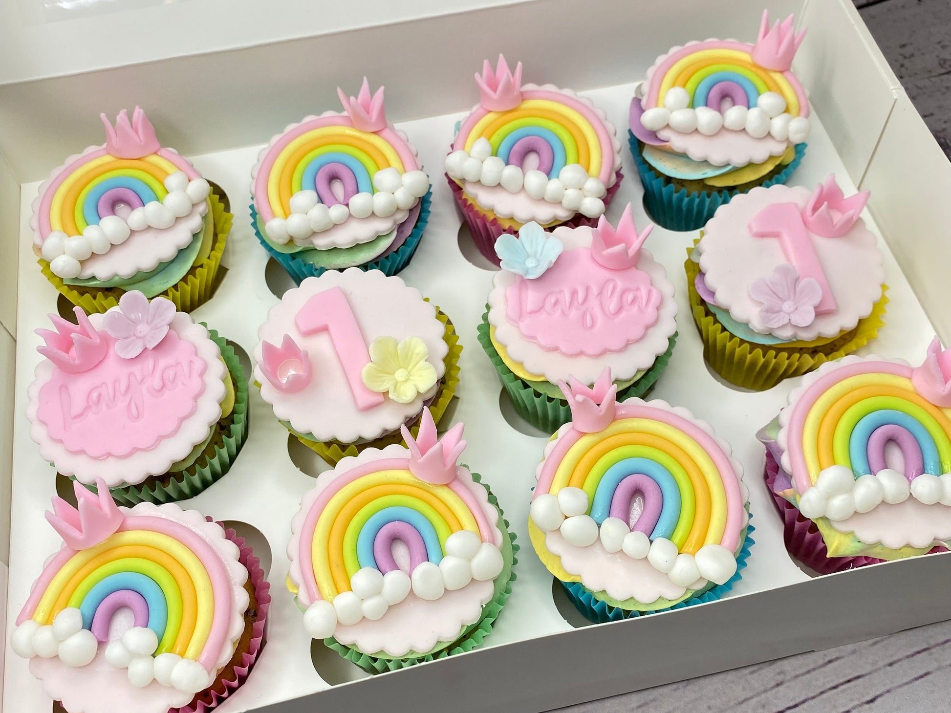 Box of cupcakes with rainbow and birthday-themed decorations 